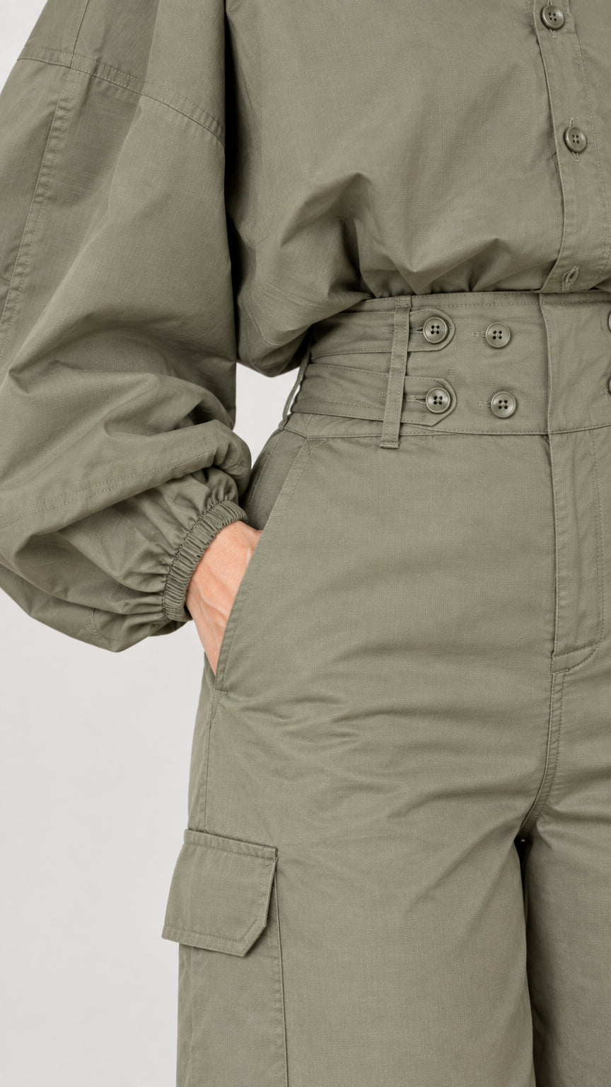 Close-up detail of side pocket, wide waistband, and balloon sleeve cuff on olive green jumpsuit
